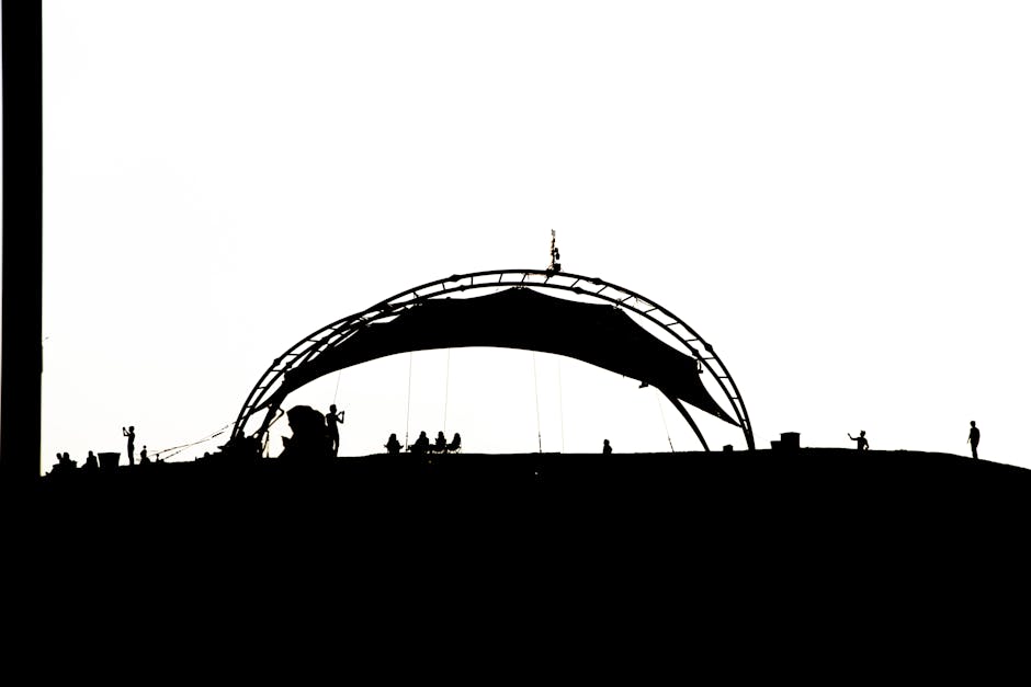 A dramatic silhouette of a structural arch on a hill at sunset, featuring people in the distance.